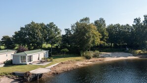 A lakeside house with a dock extending into the water, surrounded by trees and a grassy area. - Luxe Chalet w/ Sauna (Hoge Hexel)