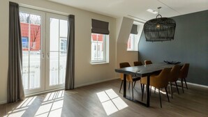 A modern dining area with a large table and chairs, a hanging light fixture, and large windows with curtains. - Luxury Apartment in Koudekerke With Sauna (Koudekerke)