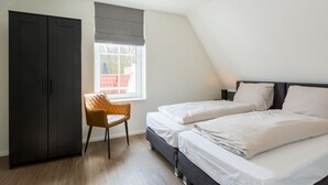 A bedroom with two beds, a wardrobe, a chair, and a window. - Luxury Apartment in Koudekerke With Sauna (Koudekerke)