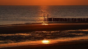 A sunset over a beach with a wooden pier extending into the water. - Luxury Apartment in Koudekerke With Sauna (Koudekerke)