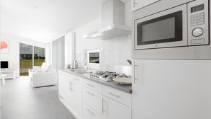 A modern kitchen with white cabinetry, a stainless steel microwave, and a large window overlooking a garden. - Nice Chalet with Fireplace near Oosterschelde (Wemeldinge)