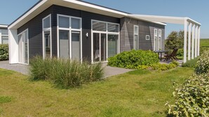 A modern house with a large glass door, a covered patio, and a well-maintained lawn. - Nice Chalet with Fireplace near Oosterschelde (Wemeldinge)