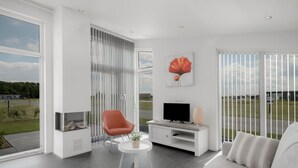 A modern living room with a large window, a red chair, a white sofa, and a flat-screen TV. - Nice Chalet with Fireplace near Oosterschelde (Wemeldinge)