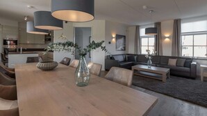 A modern living room with a wooden dining table, leather sofas, and a large vase with greenery.