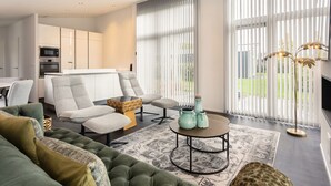 A modern living room with a sofa, armchair, and coffee table. There is a kitchen in the background with white cabinets and a microwave. - House in Zeeland Near Oosterschelde (Wemeldinge)