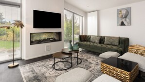 A modern living room with a green sofa, a fireplace, a flat-screen TV, and a large window with blinds. - House in Zeeland Near Oosterschelde (Wemeldinge)