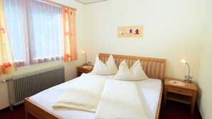 Habitación de hotel con una cama grande, dos mesitas de noche, una ventana con cortinas, un radiador y un cuadro colgado en la pared.