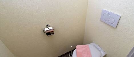 A small, narrow bathroom with a toilet, a towel rack, and a toilet paper holder.