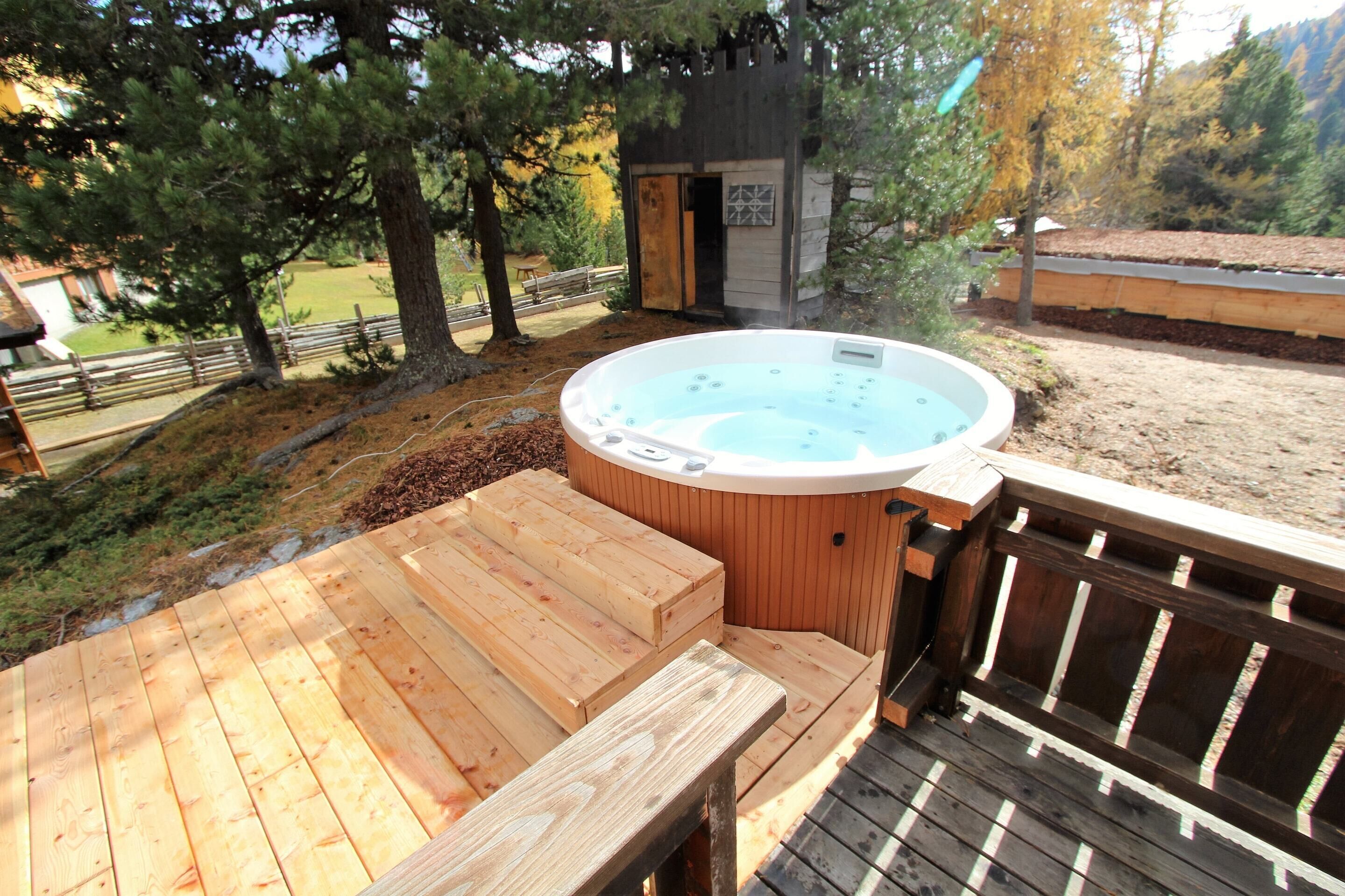 Ein Whirlpool auf einer Holzterrasse, mit Holzzaun und Bäumen im Hintergrund.