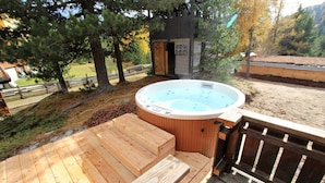 Un jacuzzi en una terraza de madera, con un cerco de madera y árboles al fondo.