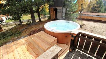 Ein Whirlpool auf einer Holzterrasse, mit Holzzaun und Bäumen im Hintergrund.