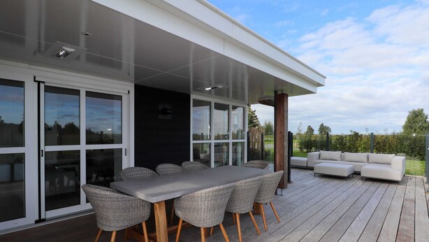 An outdoor patio with a dining table and chairs, a sofa, and a covered area with glass doors. - Luxury Villa with Sauna & Hot Tub at Lake (Delfstrahuizen)