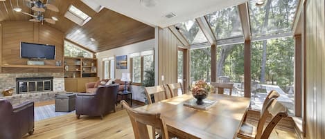 A spacious living area with a wooden ceiling, a fireplace, and a large dining table with chairs.