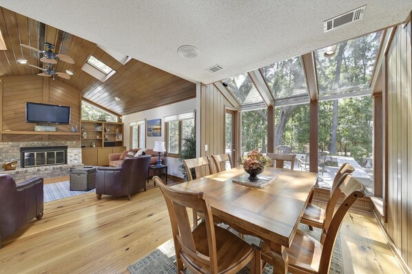 Un vaste espace de vie doté d’un plafond en bois, d’une cheminée et d’une grande table à manger avec des chaises.