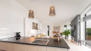 A modern kitchen with a central island, stainless steel appliances, pendant lighting, and a view of the living area. - Chalet in Zeeland With Garden and Fireplace (Wemeldinge)