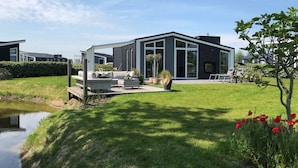 A modern house with a large patio, a pond, and a well-maintained lawn. - Chalet in Zeeland With Garden and Fireplace (Wemeldinge)