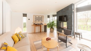 A modern living room with a sofa, a coffee table, a TV mounted on a stone wall, and a fireplace. - Chalet in Zeeland With Garden and Fireplace (Wemeldinge)