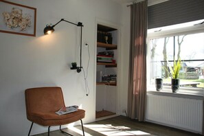 Een kamer met een bruine stoel, een bureau, een boekenkast, een raam met gordijnen en een radiator.