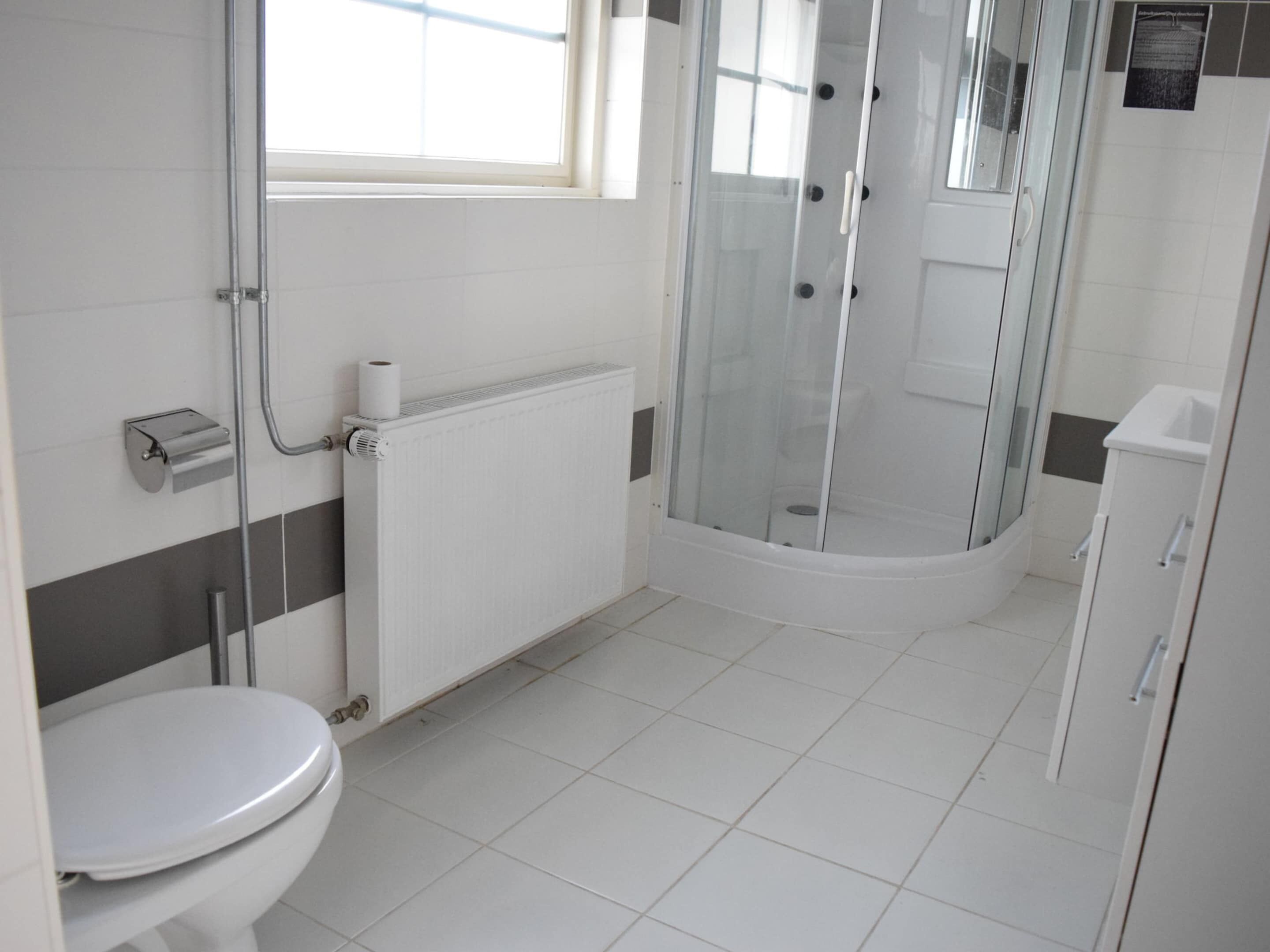 A modern bathroom with a toilet, a shower enclosure, and a radiator.