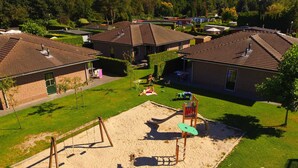 Zona residencial con un parque infantil que incluye columpios y un tobogán, rodeada de casas con techos inclinados.