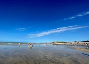 A beach with people walking along the shore, a clear sky, and distant cliffs. - Cottage in Le Bourg-dun Near the Sea (Le Bourg-Dun)