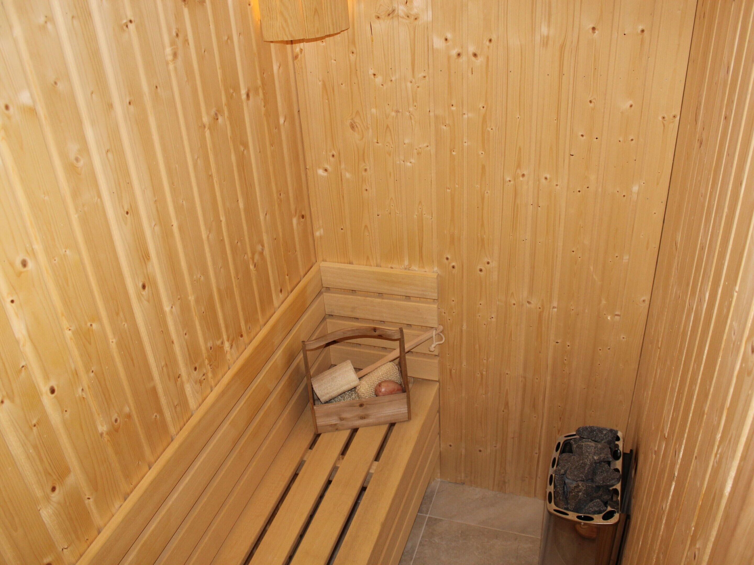Eine Holzsauna mit Sitzbank, Ablagefläche und einem Behälter gefüllt mit Steinen.
