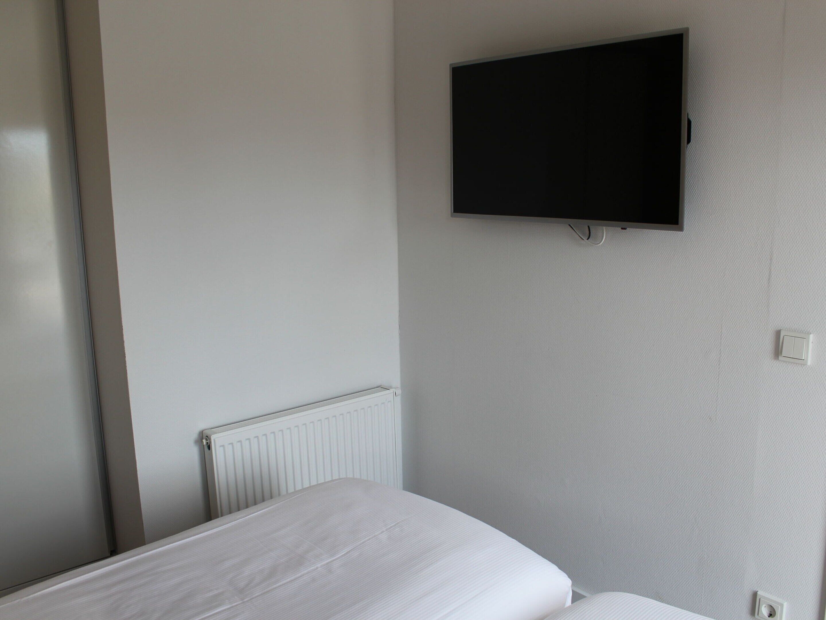 A bedroom with a bed, a wall-mounted TV, and a radiator.