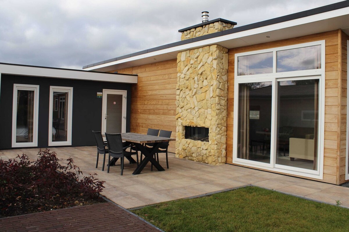 A modern house with a stone exterior, a large sliding glass door, and a patio with a table and chairs.