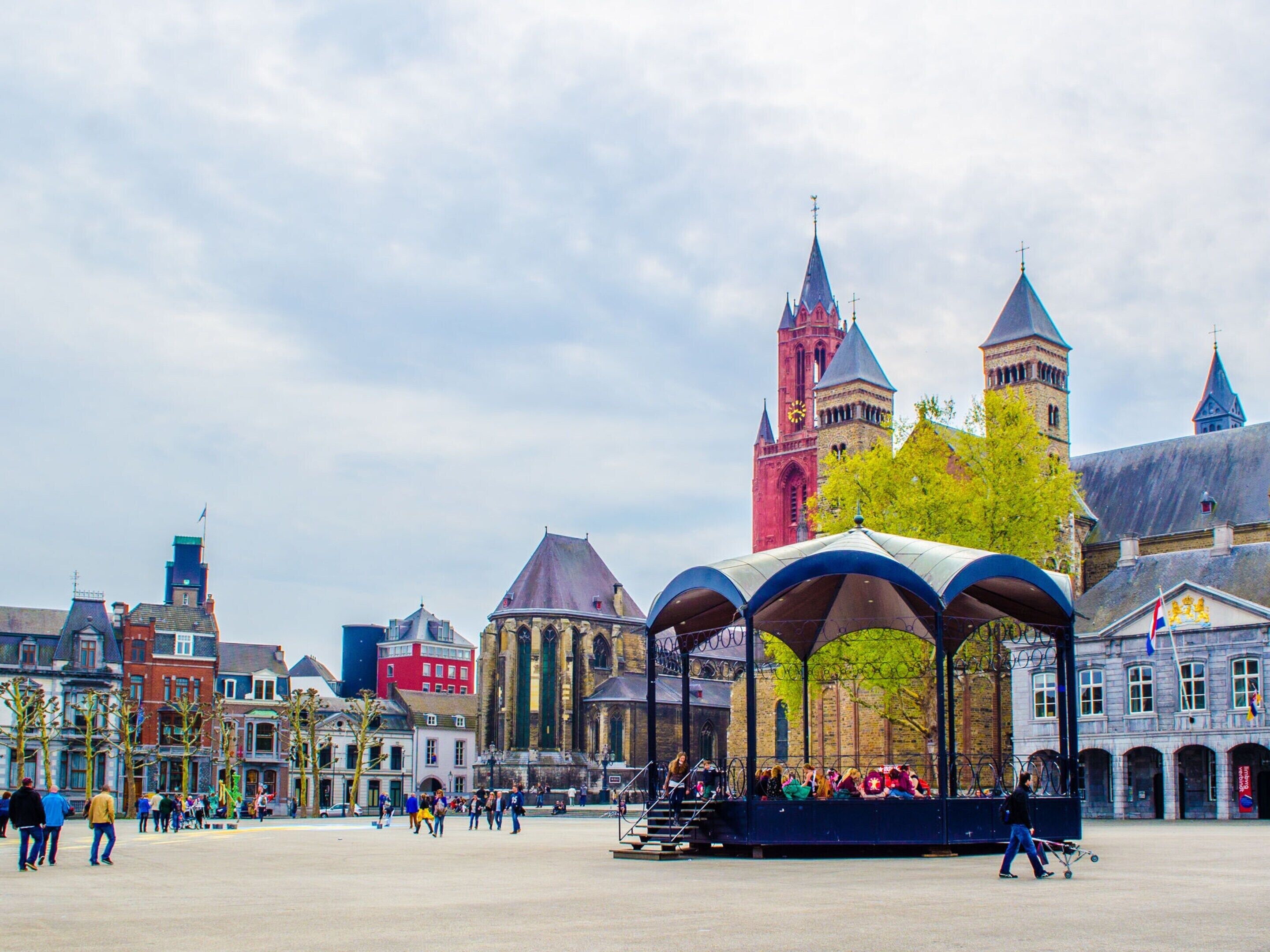 A historic square with a prominent church tower, a covered seating area, and traditional buildings.