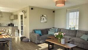 Ein modernes Wohnzimmer mit grauem Sofa, einem Holztisch und einem Essbereich mit Holztisch und Stühlen.