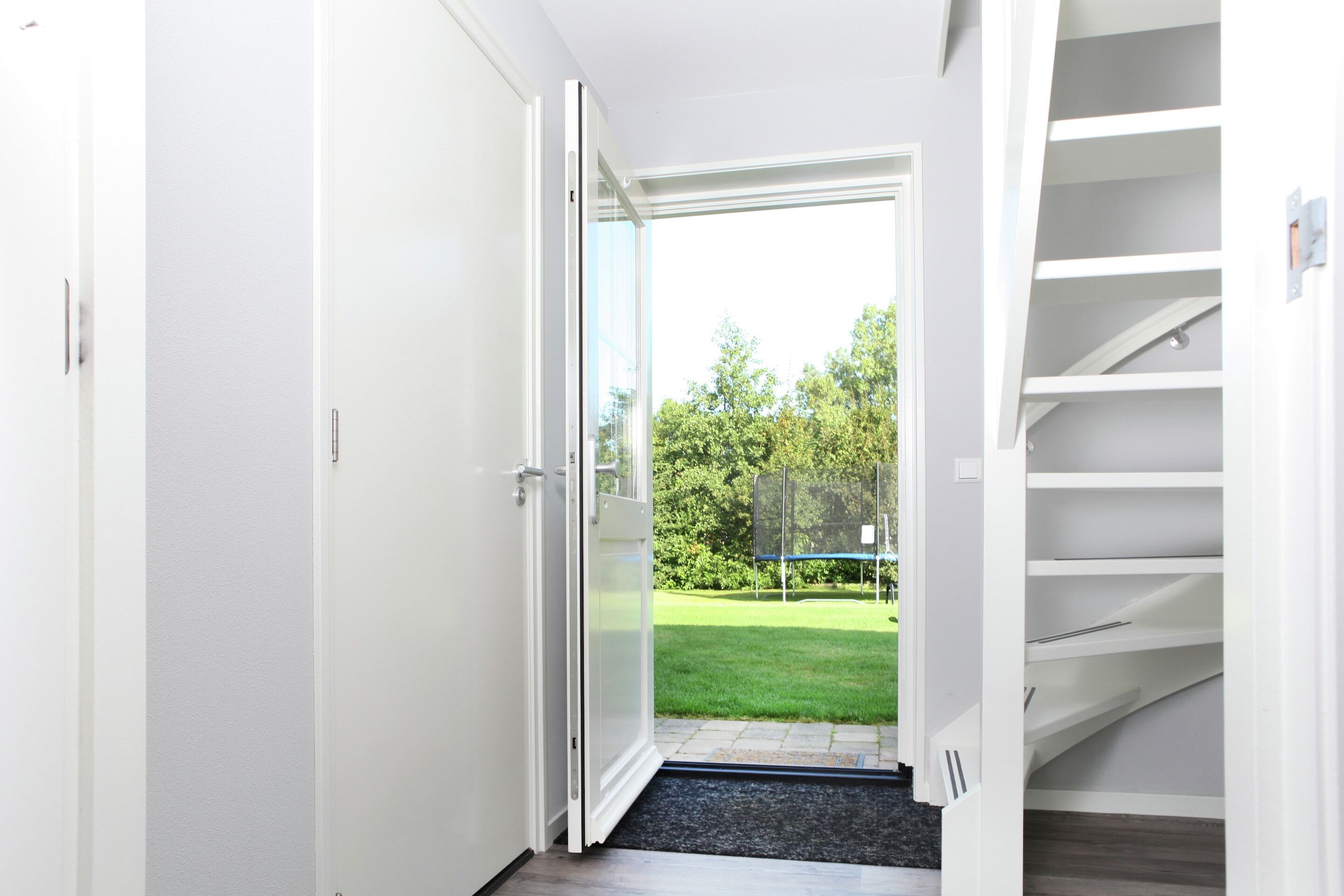 Um corredor com uma porta de vidro deslizante que dá para um quintal com um trampolim.