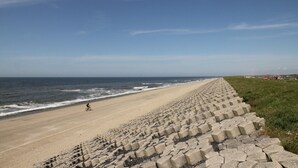 Une plage avec un mur de protection en béton le long du littoral et un cycliste sur la piste.
