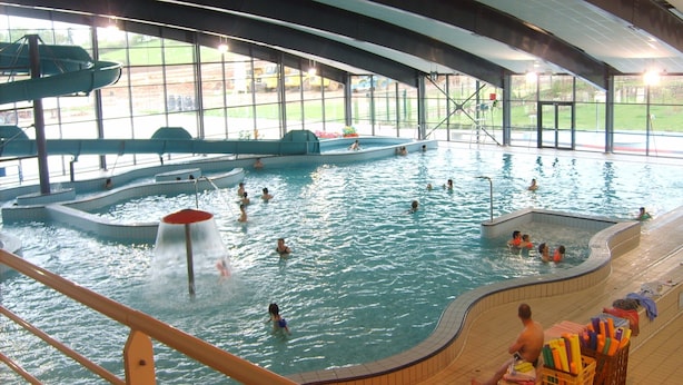 An indoor swimming pool with multiple lanes, a water slide, and a viewing area with chairs.