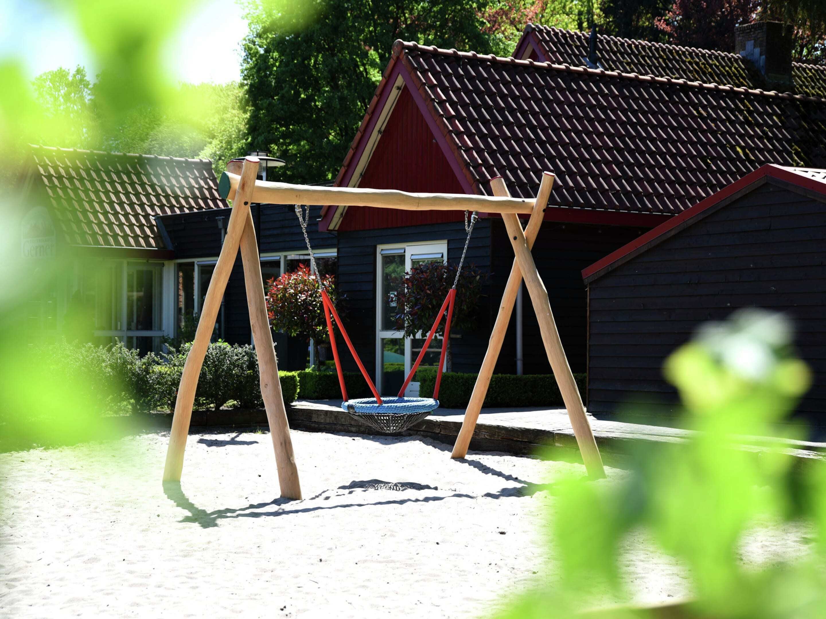 A wooden swing set in a garden with a house in the background.