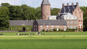 A large, historic building with a prominent tower and multiple chimneys, surrounded by a well-maintained green field with cows grazing. - Attractive Holiday Home with Large Garden near Zwolle (Dalfsen)