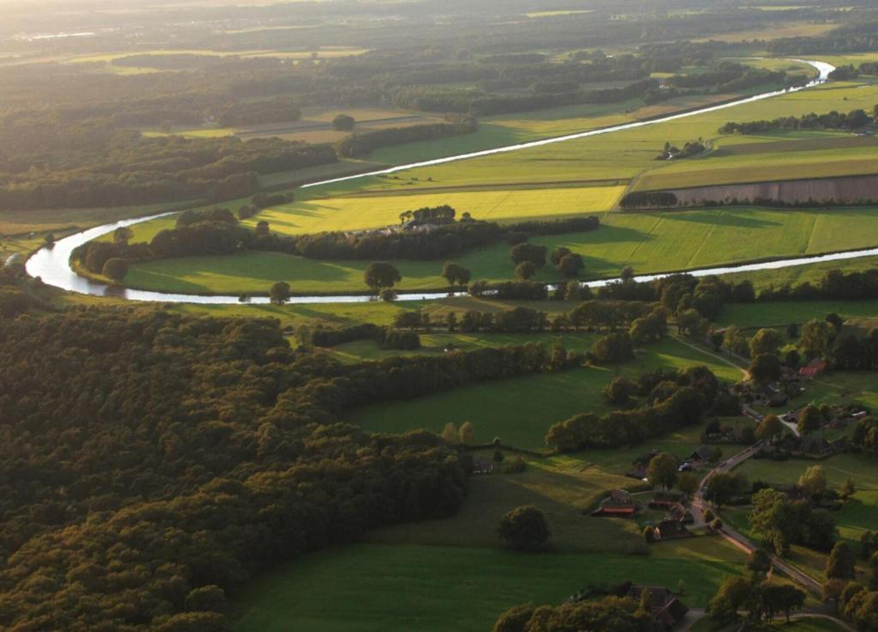 An aerial view of a rural landscape with a river meandering through fields, surrounded by trees and small buildings.