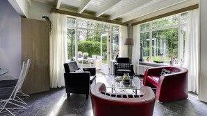 A sunlit room with a glass table, two red chairs, a black chair, and a glass coffee table. - Attractive Holiday Home with Large Garden near Zwolle (Dalfsen)