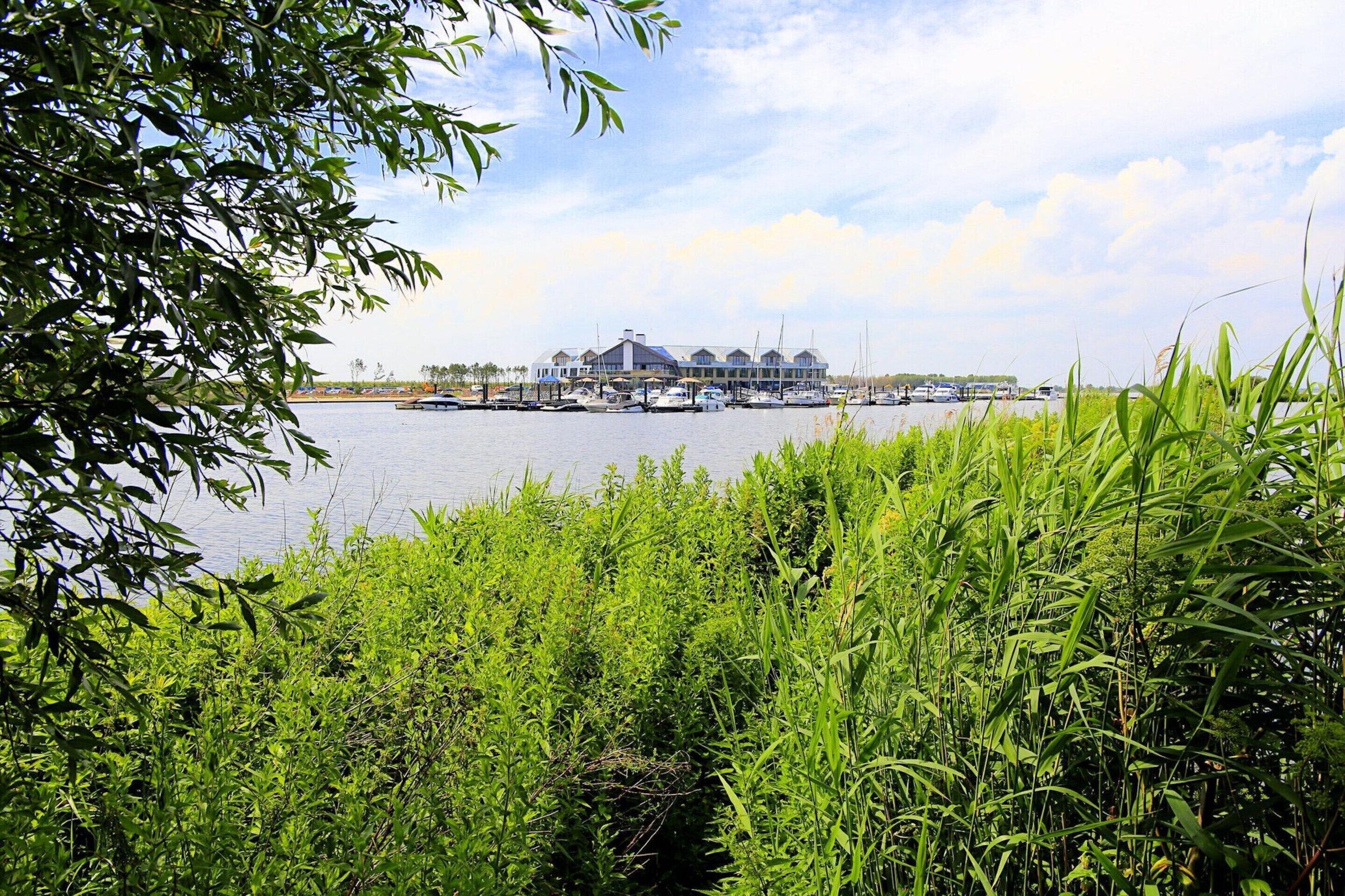 A marina with boats docked, a large building with a covered area, and lush greenery in the foreground.