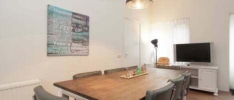 Un comedor con una mesa de madera, seis sillas, un televisor y una pared decorada con un cartel motivacional.