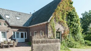 A brick house with a sloped roof, a small patio with chairs, and a green door. - Holiday Home in Bergen Near North Sea Beach (Bergen aan Zee)