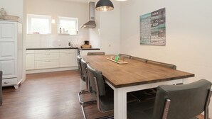 A modern kitchen with white cabinets, a wooden dining table, and two pendant lights. - Holiday Home in Bergen Near North Sea Beach (Bergen aan Zee)