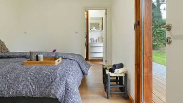 A bedroom with a bed, a bedside table, a chair, and a view of a bathroom and outdoor area.