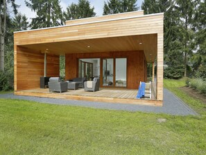 Una moderna baita in legno con un portico coperto, posti a sedere all'aperto e una porta vetrata che conduce a un'area privata.