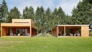 A modern two-story house with a covered patio area, large windows, and a well-maintained lawn. - Bright & Airy Forest Cabin (Enter)