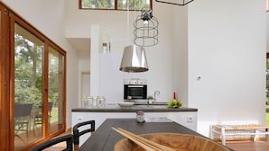 A modern kitchen with a wooden dining table, black chairs, and a large wooden bowl. - Bright & Airy Forest Cabin (Enter)
