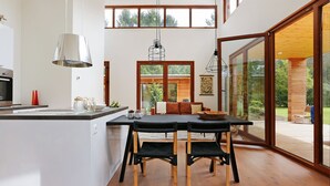 A modern kitchen with a large island, wooden flooring, and a dining area with a table and chairs. - Bright & Airy Forest Cabin (Enter)