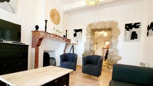 A living room with a TV, two armchairs, a sofa, a wooden table, and a stone archway. - Village House in La Caunette With Pool (La Caunette)