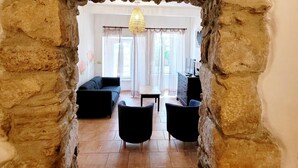 A room with a stone archway, a sofa, two armchairs, a TV, and a chandelier. - Village House in La Caunette With Pool (La Caunette)