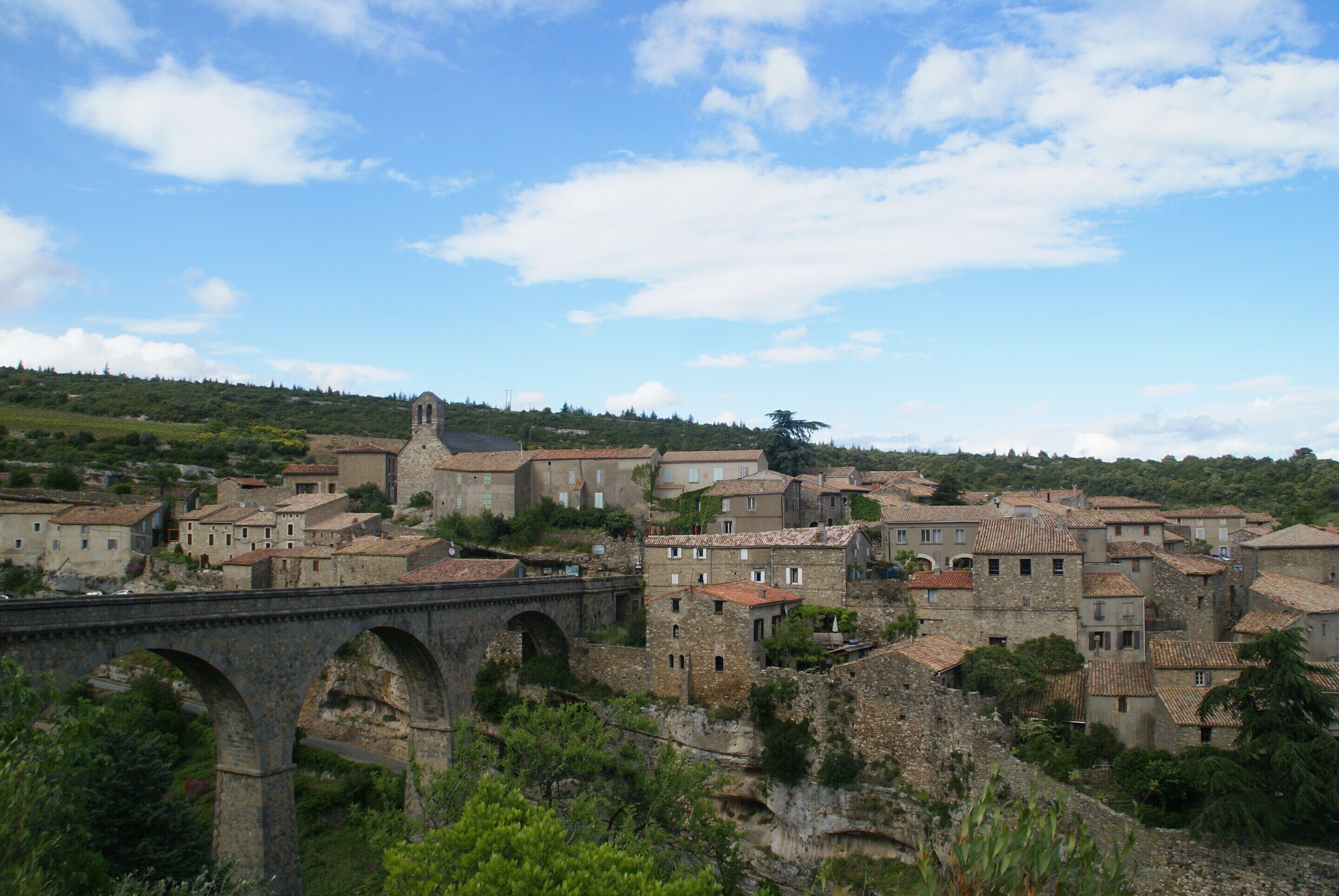 A historic town with stone buildings, a bridge, and a hill in the background.
