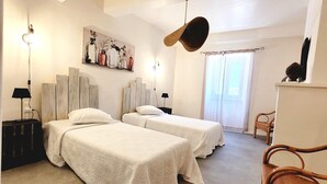 A hotel room with two beds, a painting on the wall, a hanging hat, a chair, and a window with curtains. - Village House in La Caunette With Pool (La Caunette)